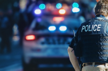 A police officer in front of a cop car with the lights on