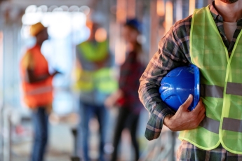 A individual standing in front of a group, holding a hard hat